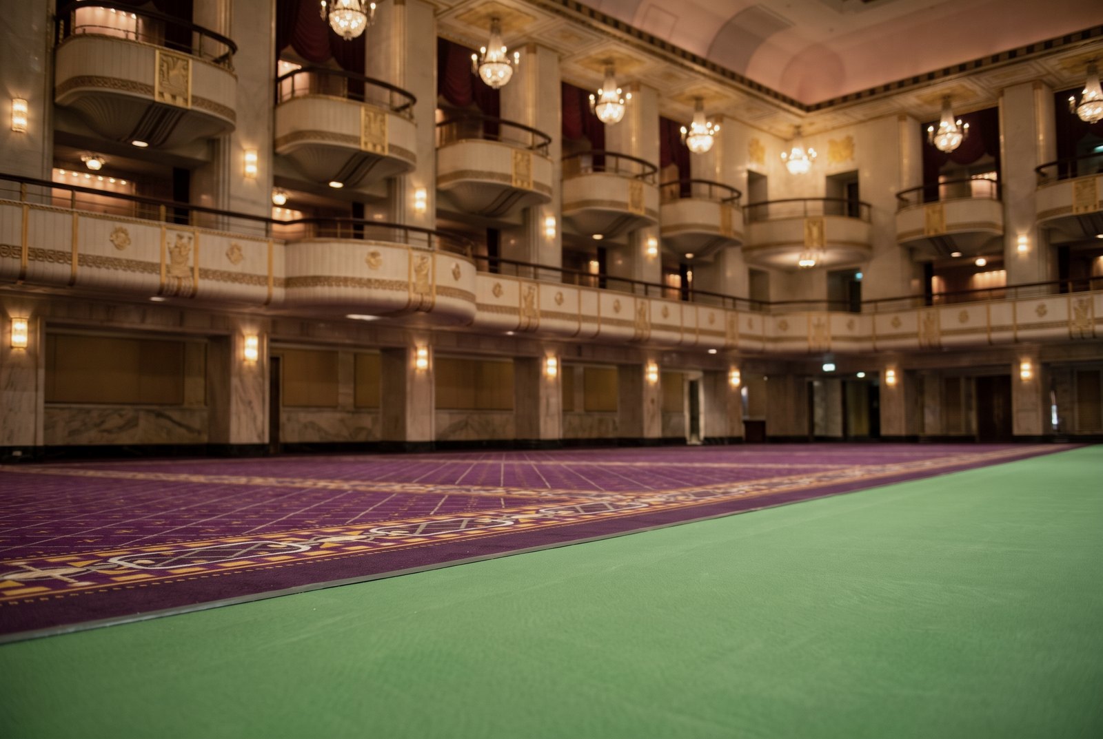 Detail of the edge of a tennis court surround meeting the original patterned purple and gold carpet of a hotel ballroom